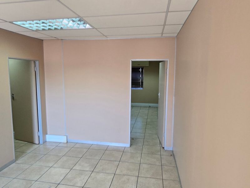 A vacant commercial office space featuring neutral painted walls, ceramic tiled flooring, and a suspended ceiling with integrated lighting.