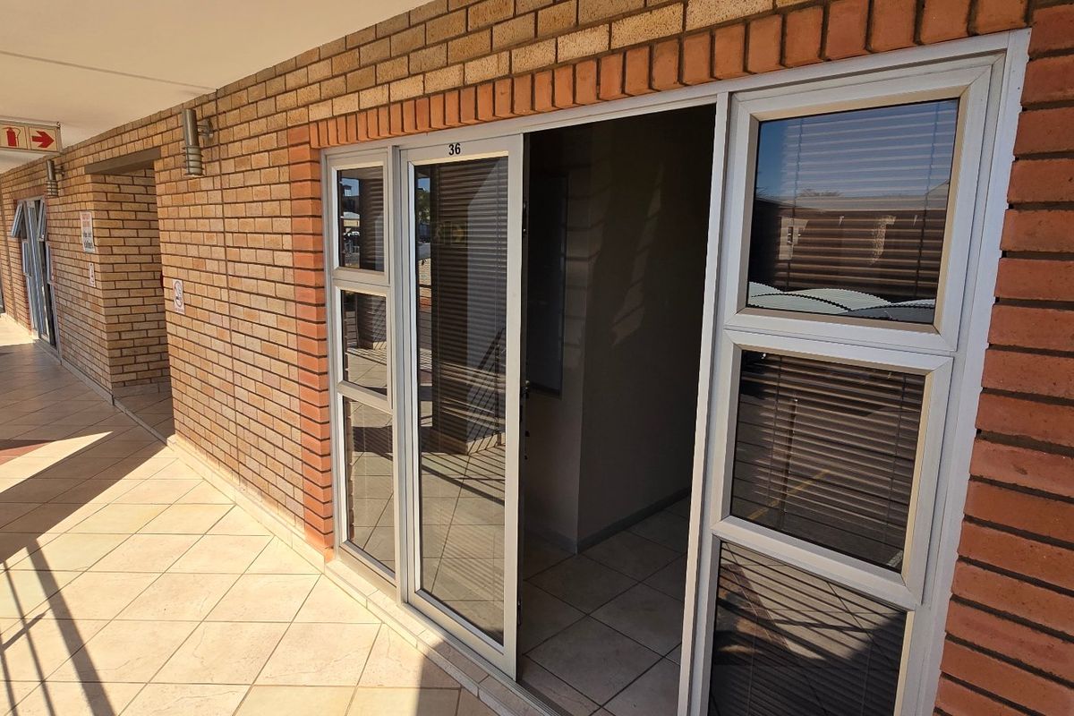 A commercial exterior walkway featuring brick facade, tiled flooring, and aluminium sliding door access to unit 36.