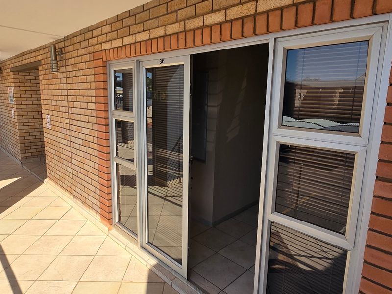 A commercial exterior walkway featuring brick facade, tiled flooring, and aluminium sliding door access to unit 36.