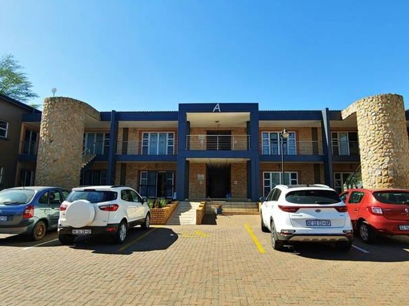 Front elevation of a commercial office building featuring stone-clad pillars, a paved parking area, and a two-story facade with balcony access.