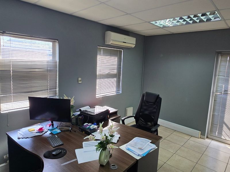 A functional commercial office space featuring tiled flooring, a suspended ceiling with recessed lighting, and a wall-mounted air conditioning unit.