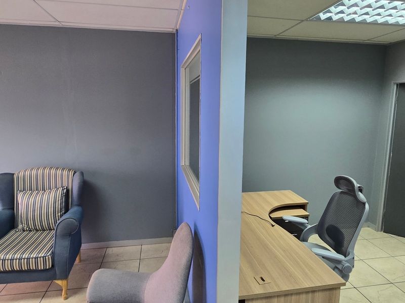 A functional commercial office space featuring tiled flooring, a suspended ceiling with recessed lighting, and a wall-mounted split-system air conditioning unit.
