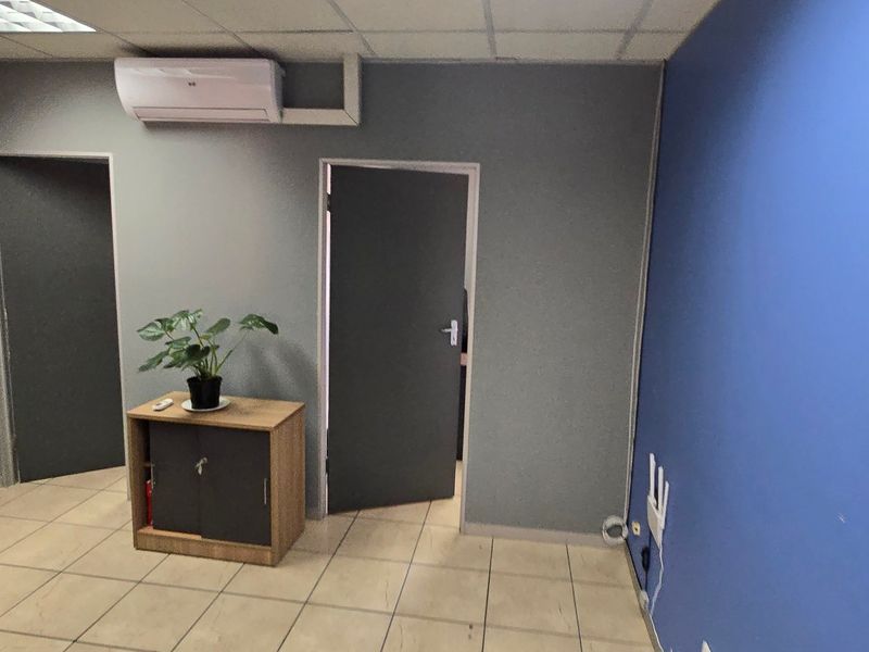 A functional office space featuring tiled flooring, a suspended ceiling, and a wall-mounted air conditioning unit.