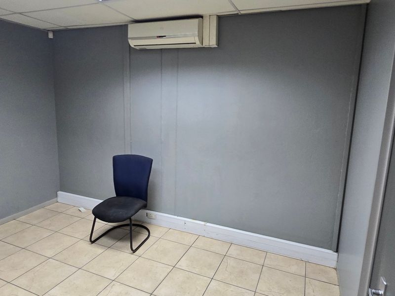 A functional office space featuring tiled flooring, a suspended ceiling, and a wall-mounted split-system air conditioning unit.