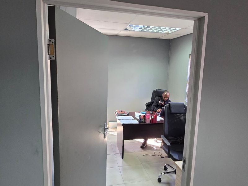 A functional commercial office space featuring tiled flooring, a suspended ceiling with integrated lighting, and an installed air conditioning unit.