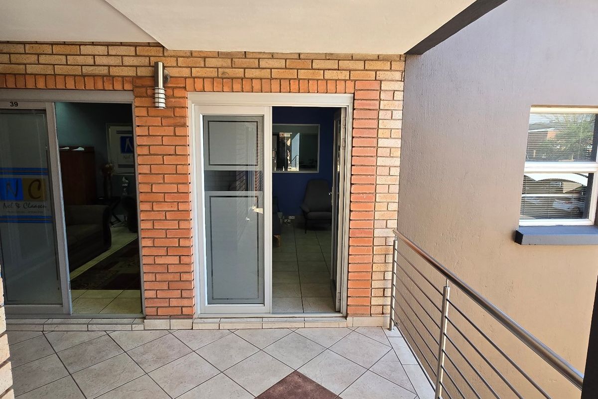 A covered balcony area featuring face brick walls, tiled flooring, and a stainless steel balustrade, providing access to the commercial office space.