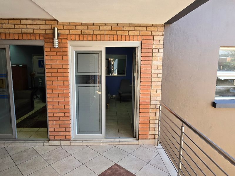 A covered balcony area featuring face brick walls, tiled flooring, and a stainless steel balustrade, providing access to the commercial office space.