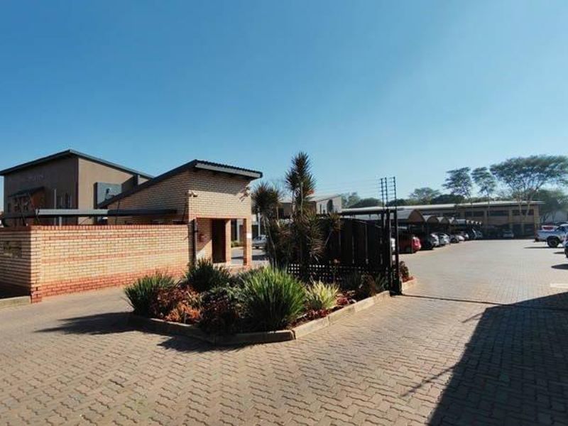 Front entrance view of a commercial property featuring a paved driveway, secure boundary wall with electric fencing, and covered parking facilities.