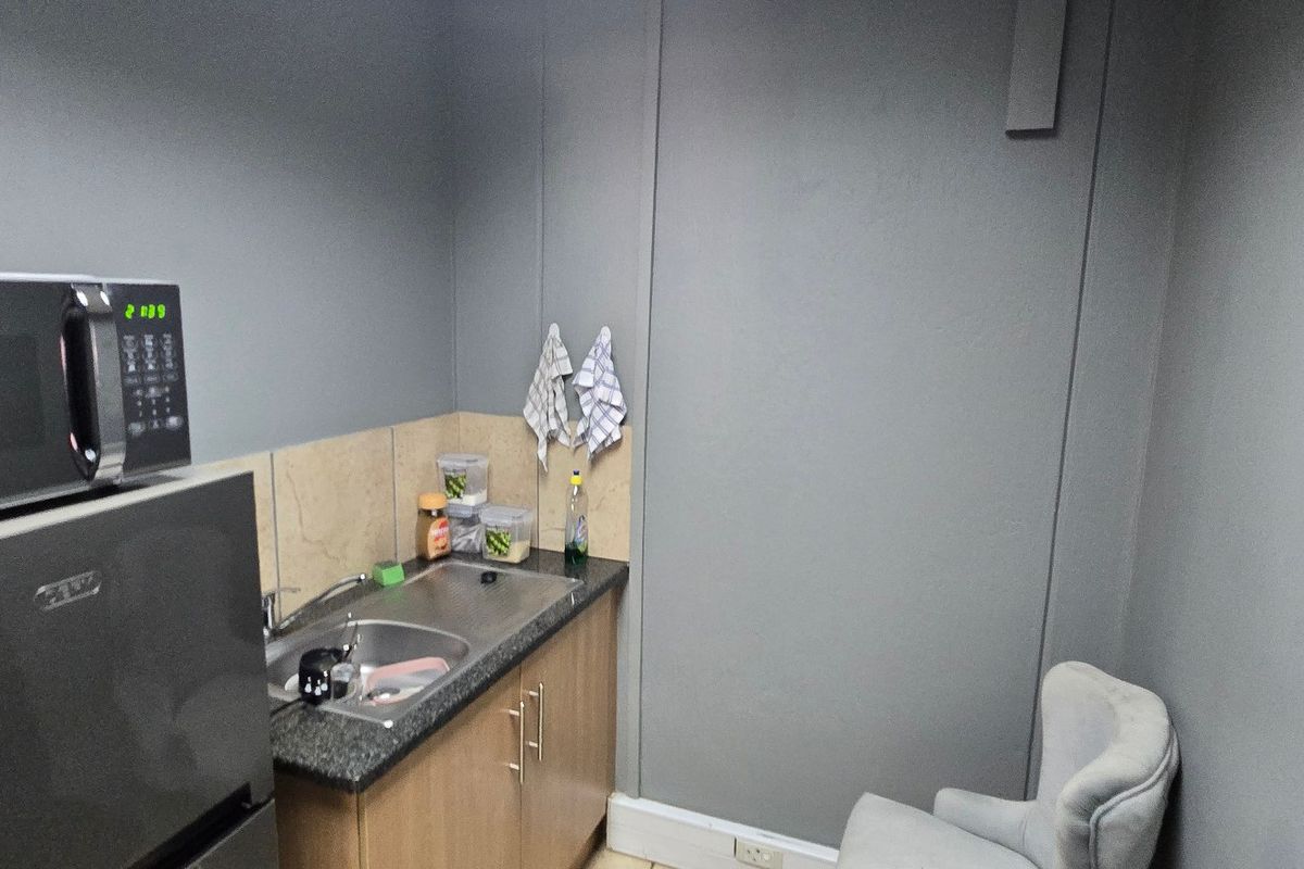 A compact kitchenette featuring built-in cabinetry, a stainless steel sink, and a tiled backsplash, suitable for office or utility use.