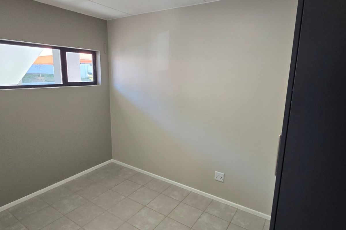 A clean, empty bedroom featuring neutral wall tones, tiled flooring, and a horizontal window, providing a versatile space ready for personalization.
