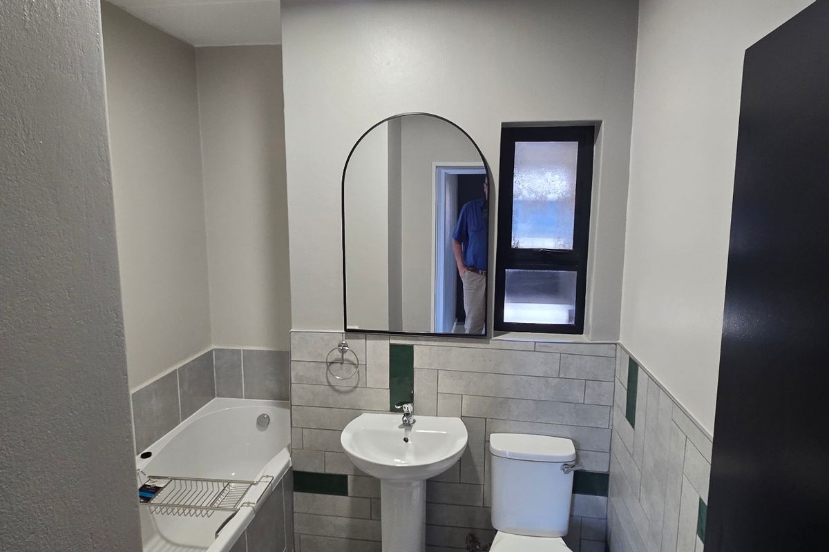 A clean and modern bathroom featuring a pedestal basin, bathtub, toilet, and stylish tiled splashback with an arched mirror.