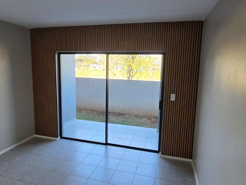 A bright, empty living area featuring modern slatted wood wall paneling, tiled floors, and a large sliding glass door leading to an outdoor patio.