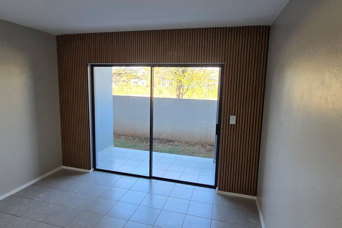 A bright, empty living area featuring modern slatted wood wall paneling, tiled floors, and a large sliding glass door leading to an outdoor patio.