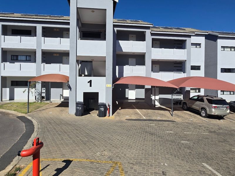 Front elevation of a multi-story apartment complex featuring paved parking areas with shade cloth carports and accessible stairwell entry points.