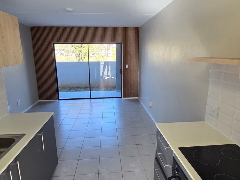 Modern open-plan kitchen and living area featuring sleek cabinetry, electric hob, tiled flooring, and a stylish slatted wood accent wall leading to a balcony.