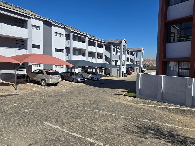 Exterior view of a modern apartment complex featuring paved parking bays with shade cloth carports and multi-story residential building facades.