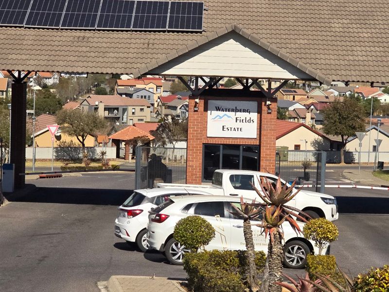 The main entrance gate and security checkpoint of Waterberg Fields Estate, featuring brick construction, tiled roofing, and integrated solar panels.
