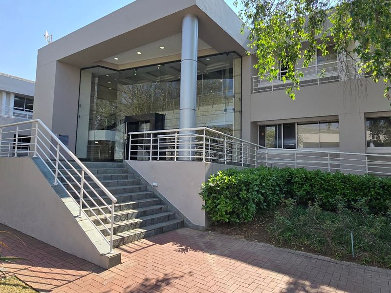 Modern commercial building entrance featuring a glass facade, concrete staircase with metal railings, and paved approach.