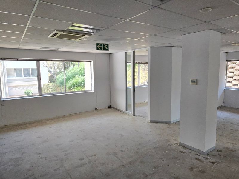 An empty, open-plan commercial office space featuring suspended ceilings, recessed air conditioning, and large windows providing natural light.