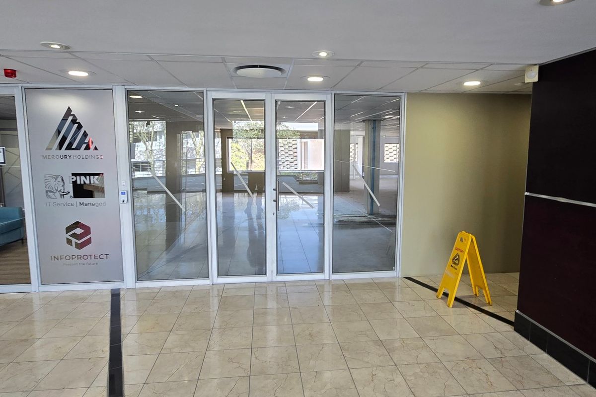A bright commercial entrance lobby featuring glass partition walls, tiled flooring, and recessed ceiling lighting, providing a professional and welcoming reception area.