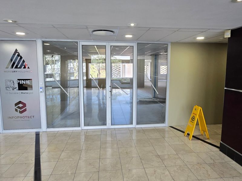 A bright commercial entrance lobby featuring glass partition walls, tiled flooring, and recessed ceiling lighting, providing a professional and welcoming reception area.