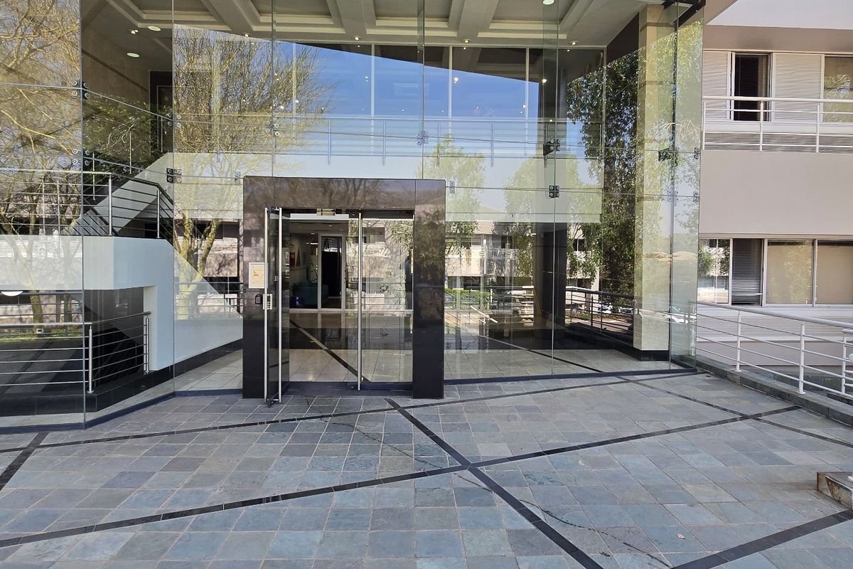 Modern commercial building entrance featuring a prominent glass facade, stone-tiled forecourt, and clean architectural lines.