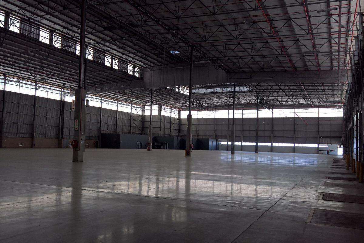 Expansive industrial warehouse space featuring polished concrete flooring, high-clearance steel truss ceilings, integrated fire sprinkler systems, and multiple roller shutter access points.