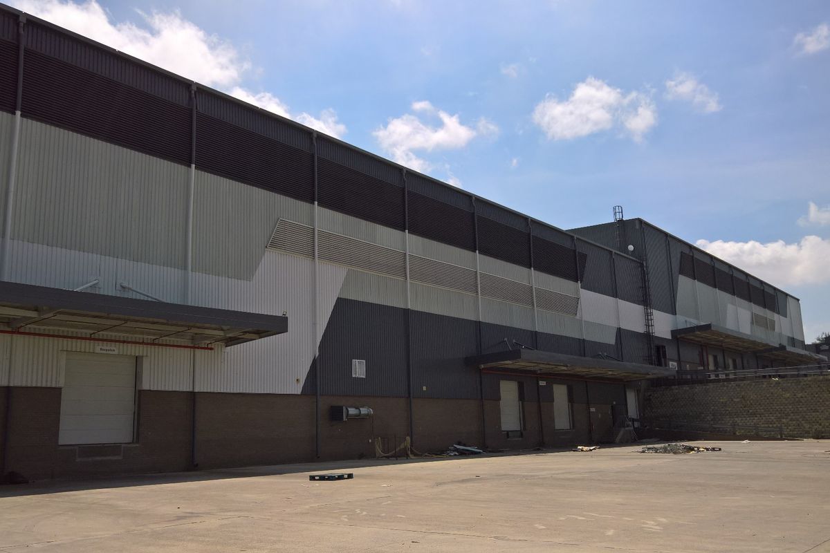 Rear view of a large industrial warehouse facility featuring metal cladding, multiple loading docks with roller shutter doors, and a spacious concrete yard.