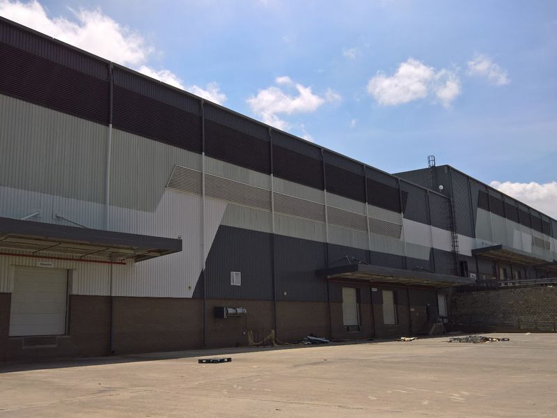 Rear view of a large industrial warehouse facility featuring metal cladding, multiple loading docks with roller shutter doors, and a spacious concrete yard.