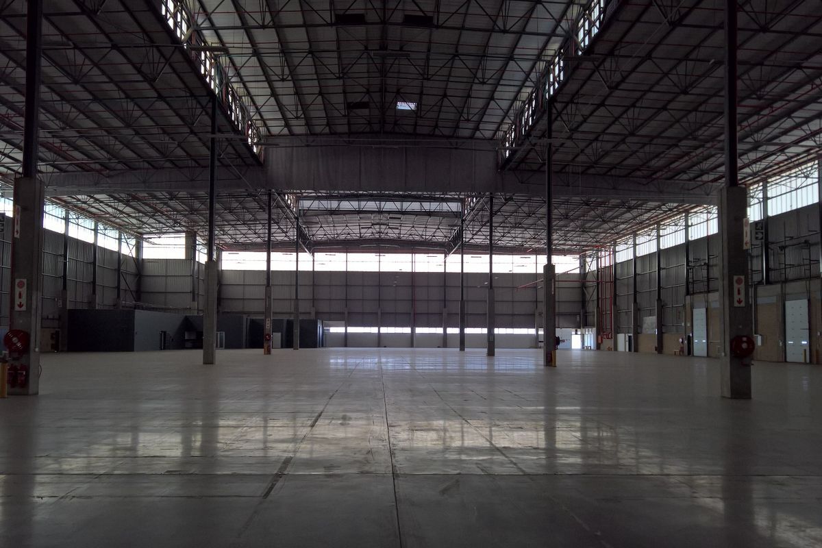 A vast, open-plan industrial warehouse space featuring high ceilings, polished concrete flooring, steel structural columns, and ample natural light from clerestory windows.