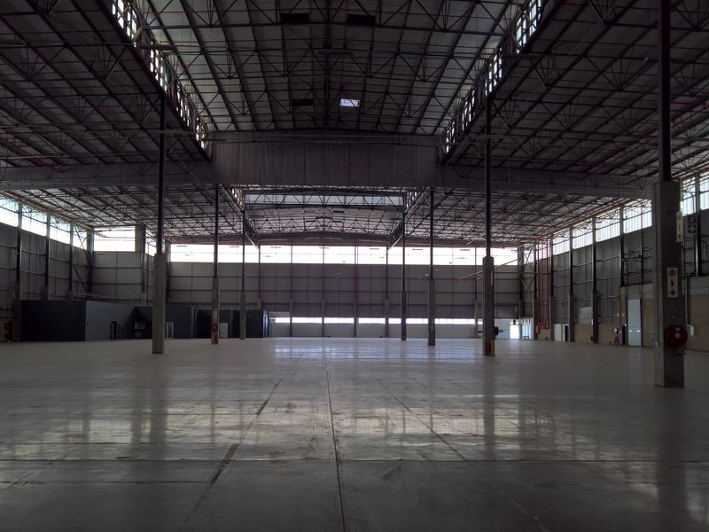 A vast, open-plan industrial warehouse space featuring high ceilings, polished concrete flooring, steel structural columns, and ample natural light from clerestory windows.