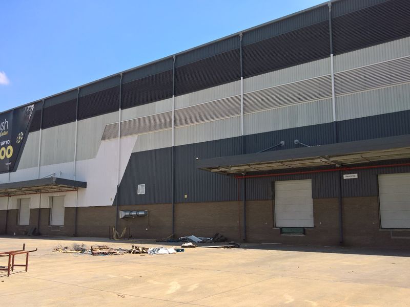 Industrial warehouse exterior featuring multiple loading bays with roller shutter doors, metal cladding, and a large concrete yard area.