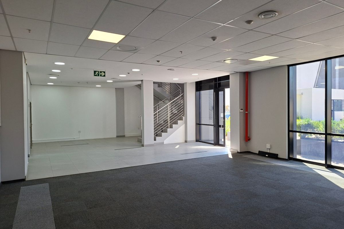 Spacious open-plan industrial office area featuring a suspended ceiling, recessed lighting, large windows, and a staircase with metal railings.