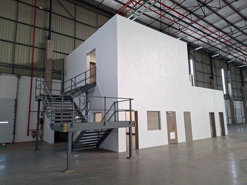 Spacious industrial warehouse interior featuring a multi-level office or utility block with an external steel staircase and high-clearance exposed roof structure.