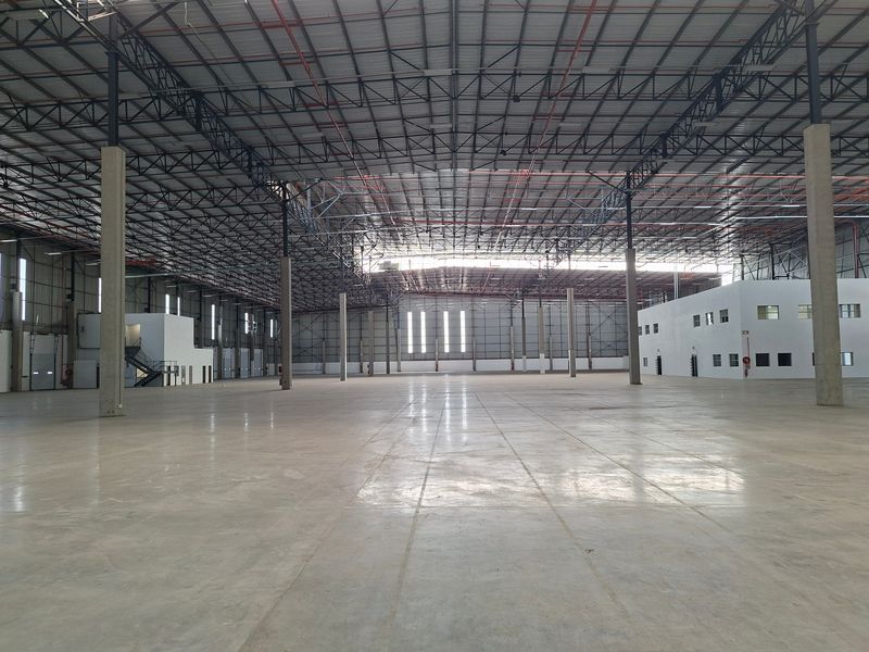 Expansive industrial warehouse space featuring high ceilings with exposed steel trusses, polished concrete flooring, and an integrated internal office structure.