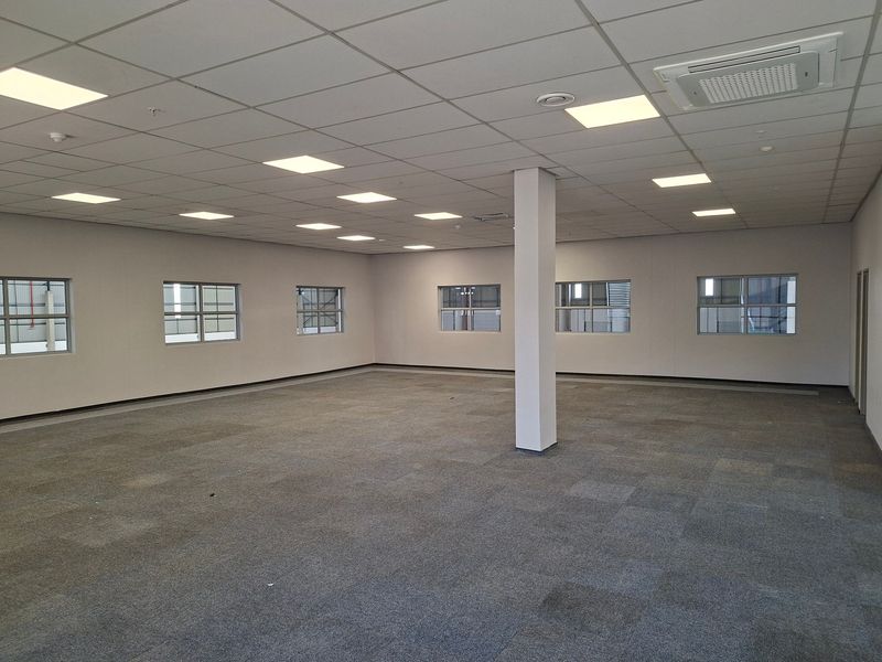 A spacious, open-plan office area featuring carpeted flooring, a suspended ceiling with recessed lighting, and integrated air conditioning.