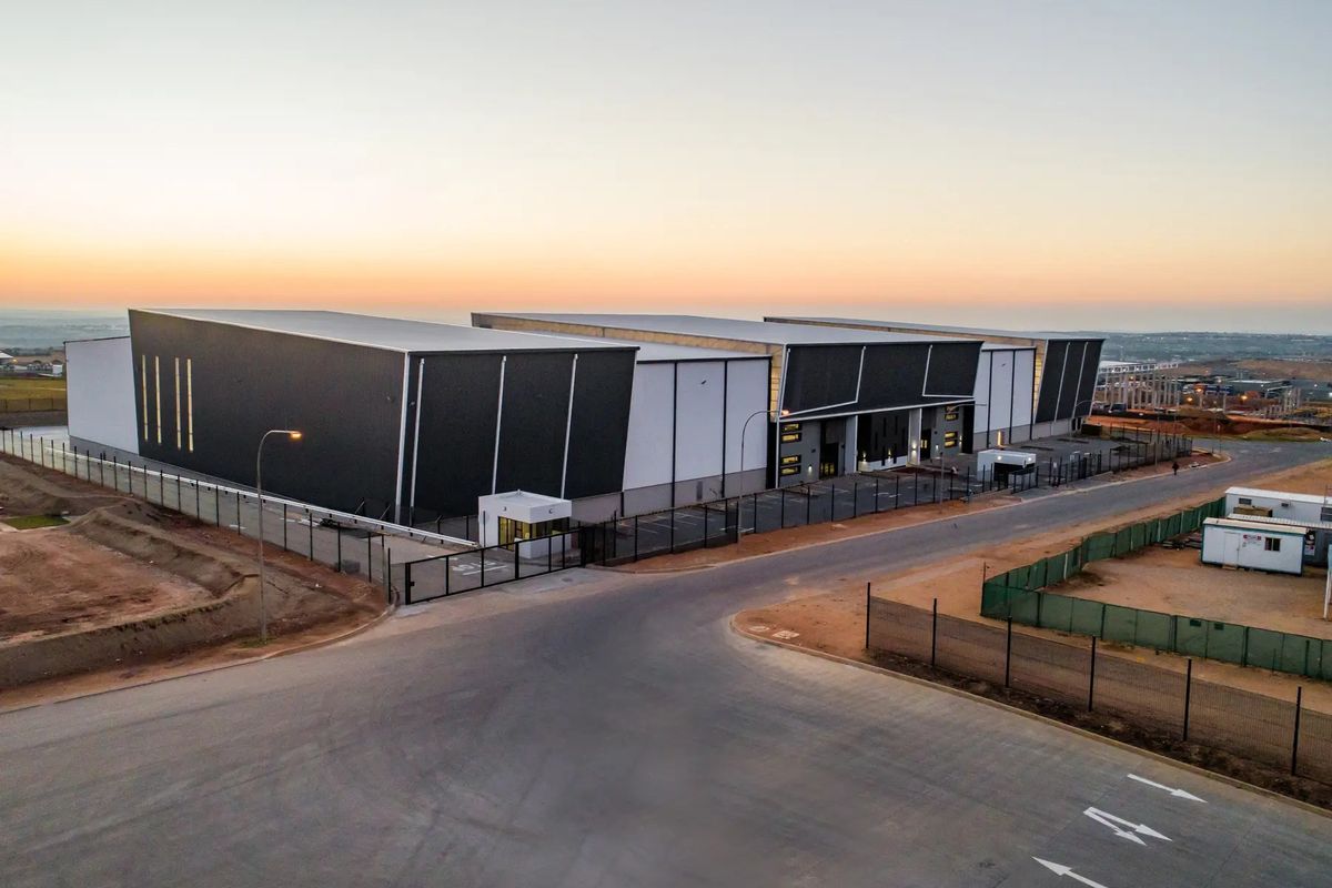 Aerial view of a modern industrial warehouse facility featuring secure perimeter fencing, a dedicated gatehouse, and extensive paved access areas.