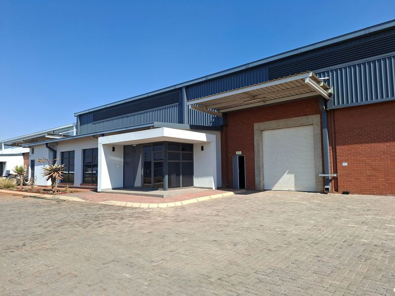 Front exterior view of an industrial property featuring a large roller shutter door, brick and metal cladding, and a paved driveway entrance.