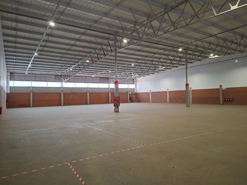 Spacious industrial warehouse featuring high ceilings with exposed steel trusses, concrete flooring, and brick wall construction, suitable for storage or manufacturing operations.