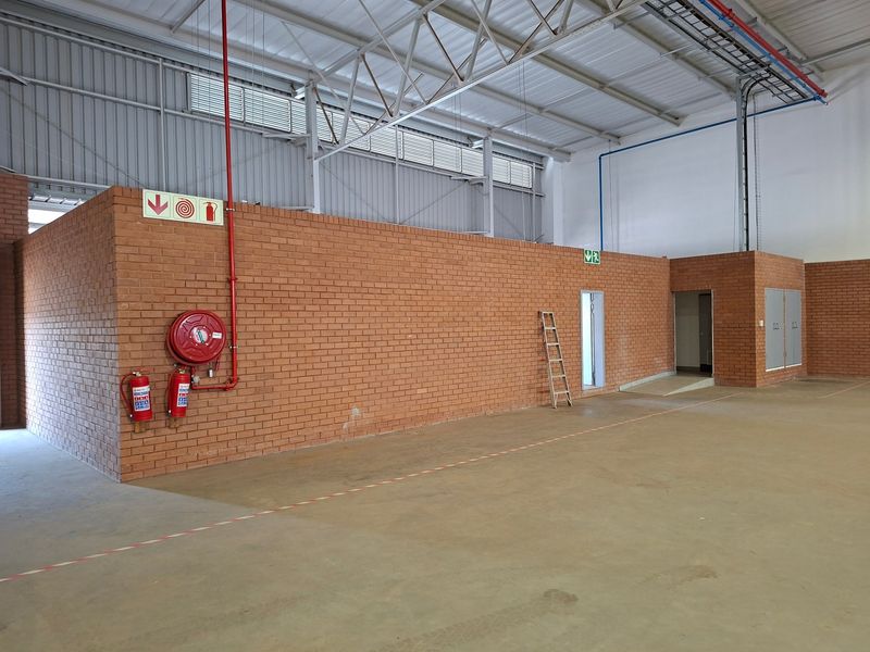 Spacious industrial utility area featuring exposed steel roof trusses, concrete flooring, and integrated fire safety equipment including a hose reel and extinguishers.