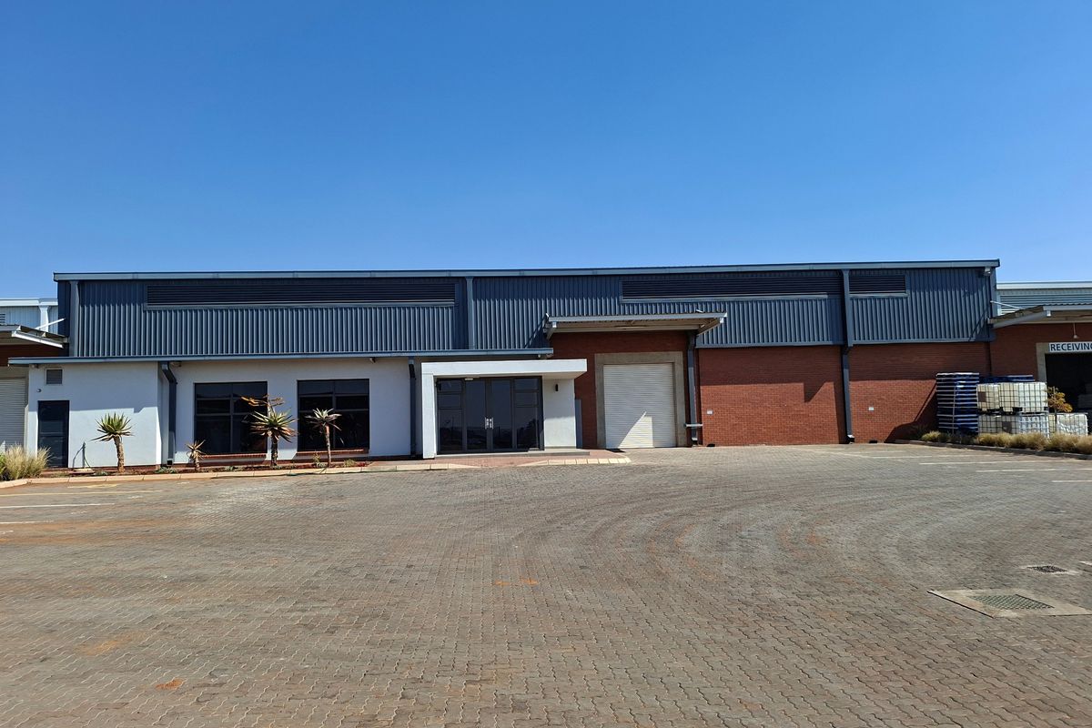 Industrial warehouse exterior featuring a large roller shutter door, brick and metal cladding facade, and a spacious paved driveway for vehicle access.