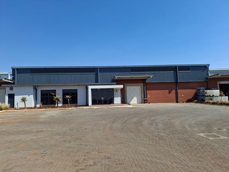 Industrial warehouse exterior featuring a large roller shutter door, brick and metal cladding facade, and a spacious paved driveway for vehicle access.