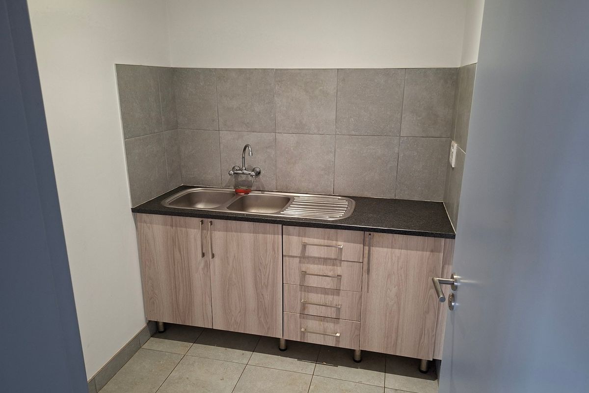 A clean and functional scullery area featuring modern laminate cabinetry, a stainless steel double sink, and neutral tiled splashback.