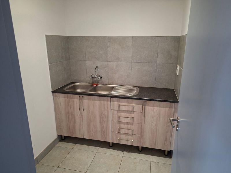 A clean and functional scullery area featuring modern laminate cabinetry, a stainless steel double sink, and neutral tiled splashback.