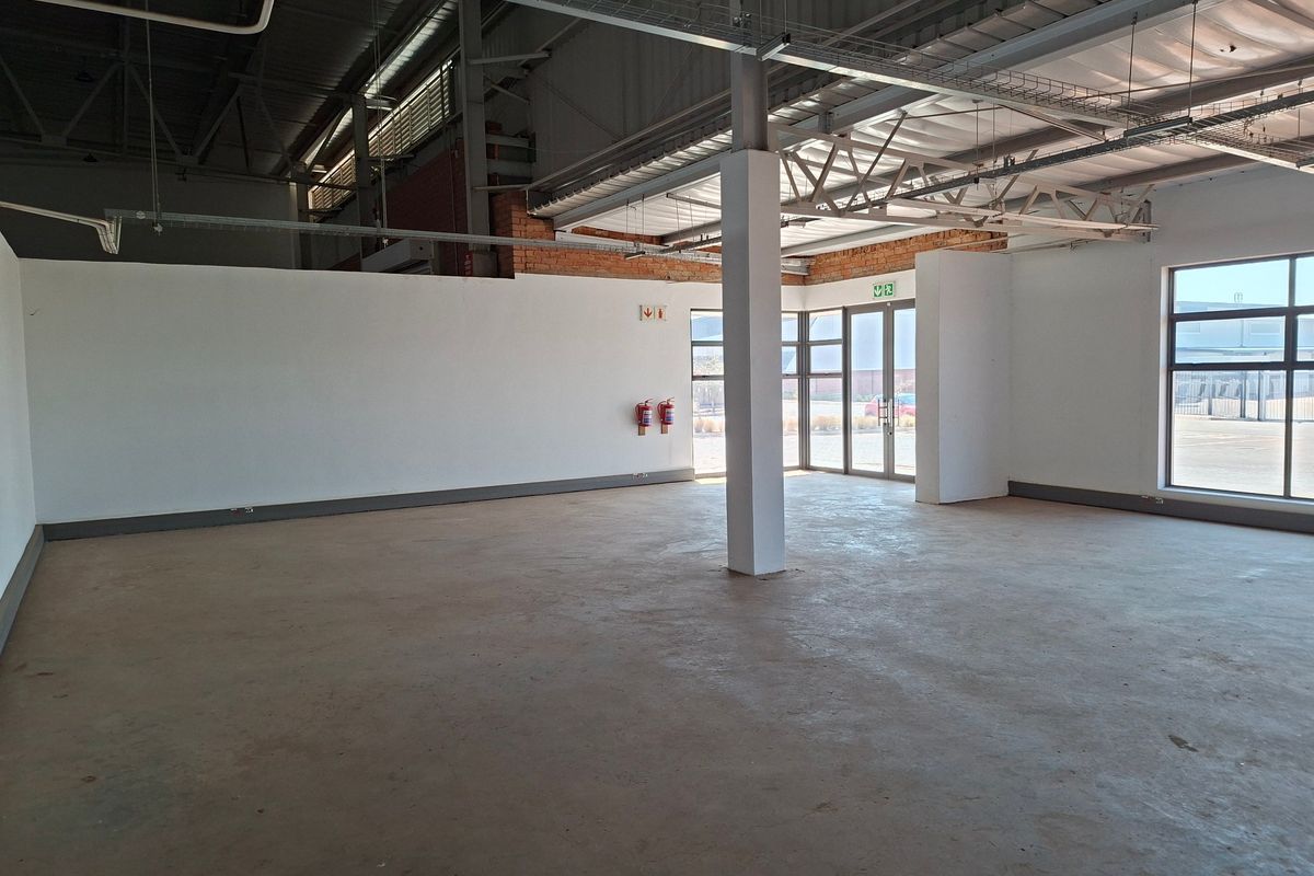 Spacious open-plan industrial unit featuring exposed steel roof trusses, polished concrete flooring, and large aluminium-framed windows providing ample natural light.