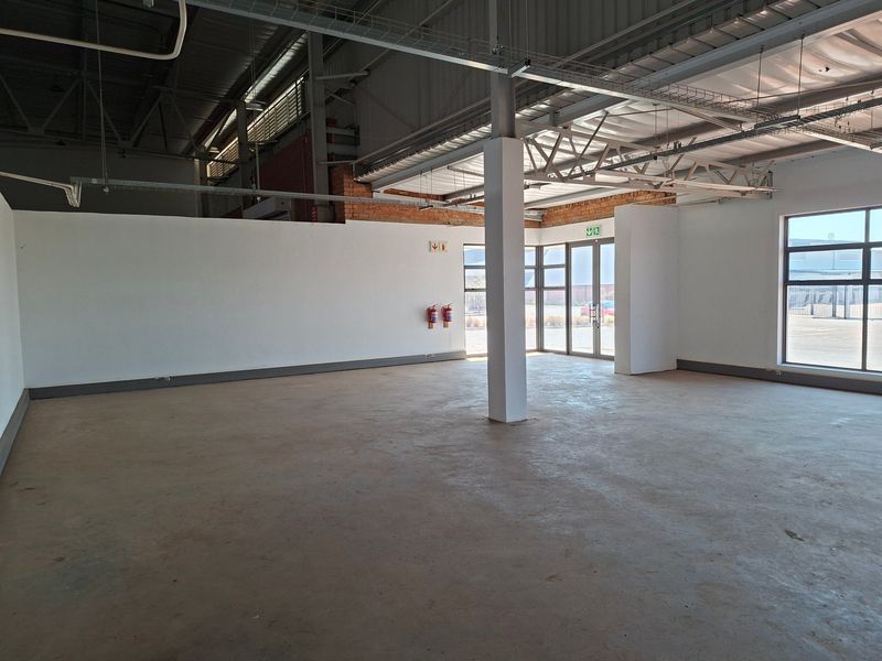 Spacious open-plan industrial unit featuring exposed steel roof trusses, polished concrete flooring, and large aluminium-framed windows providing ample natural light.