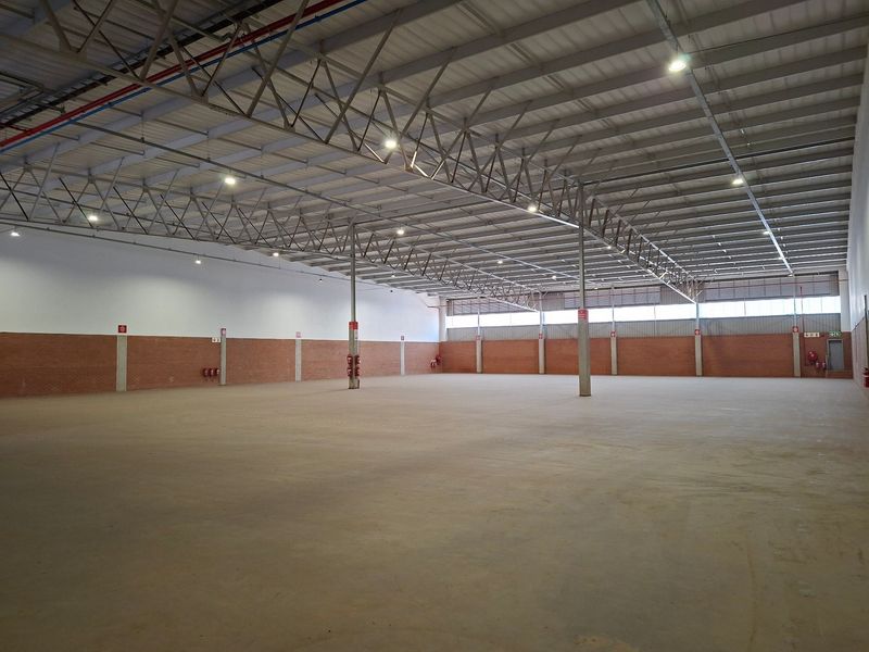 Spacious industrial warehouse unit featuring high ceilings with exposed steel trusses, concrete flooring, and brick walling, suitable for storage or manufacturing operations.