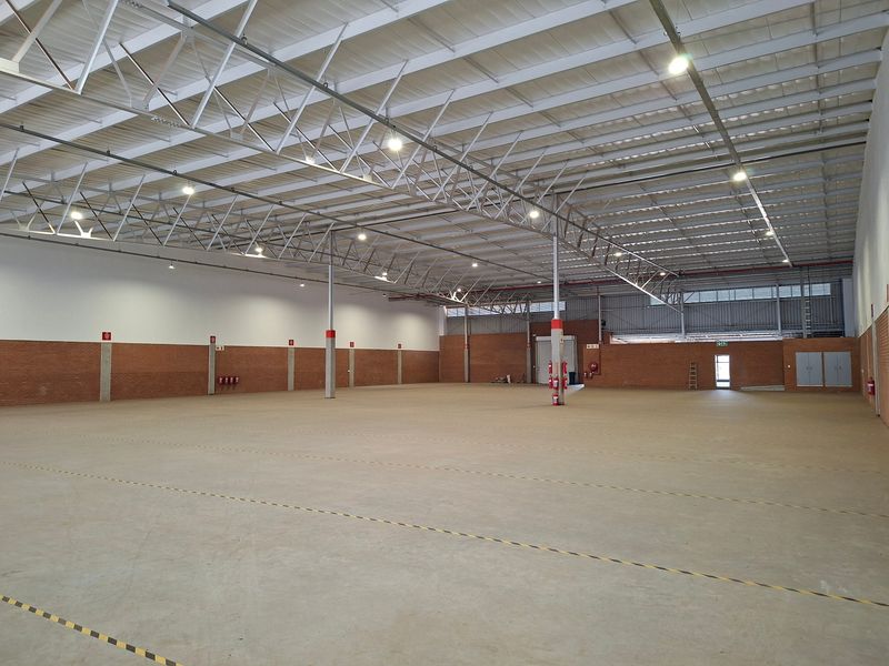 Spacious industrial warehouse featuring high ceilings with exposed steel trusses, concrete flooring, and brick wall finishes, suitable for storage or manufacturing operations.