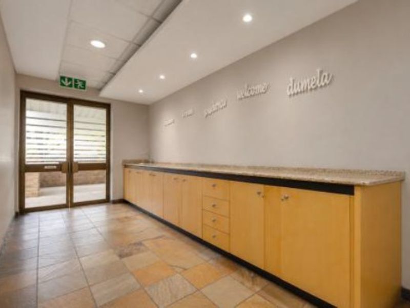 A clean, professional commercial entry area featuring built-in wooden cabinetry with stone countertops, tiled flooring, and recessed ceiling lighting.