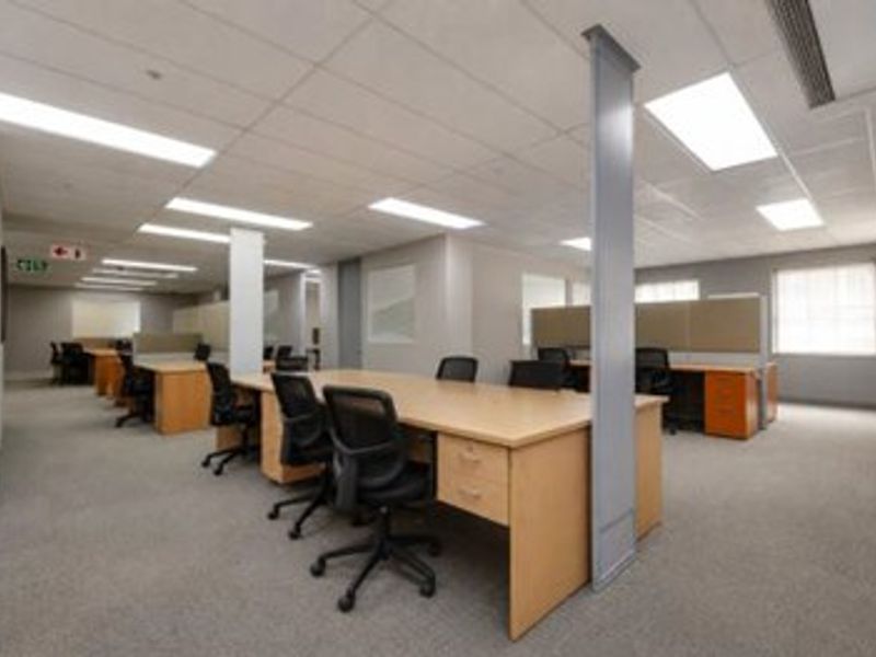 Open-plan commercial office space featuring suspended ceilings, recessed lighting, and carpeted flooring, configured with multiple workstations.